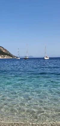 This phone live wallpaper features a group of colorful boats floating on crystal-clear blue waters against a Mediterranean beach background