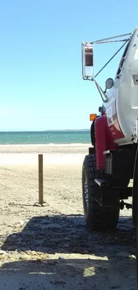 This live wallpaper depicts a large white truck on a stunning sandy beach, with bright red sand visible across the scene