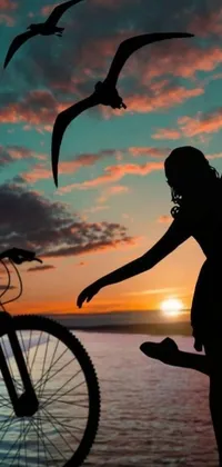 This phone live wallpaper boasts a captivating silhouette of a woman and a bicycle against a scenic body of water during sunset
