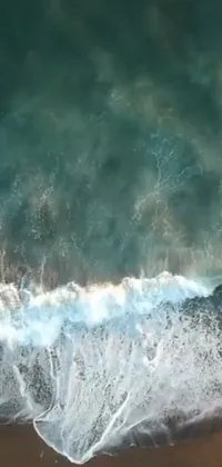 This lively phone live wallpaper features a breathtaking drone video of a surfer riding the waves on top of a sandy beach