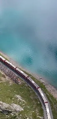 This phone live wallpaper depicts a stunning aerial view of a long train rolling along a track near a tranquil body of water