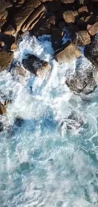 Looking for a stunning live wallpaper for your phone? Look no further than this breathtaking bird's eye view of a body of water surrounded by rocks