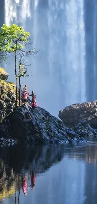 Enhance your phone's aesthetic appeal with a stunning live wallpaper depicting a group of people gazing at a cascading waterfall, aptly captured in a super wide image format