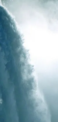 This live wallpaper depicts a stunning scene of a surfer riding a massive wave on top of a surfboard amidst a beautiful waterfall and fog-filled background