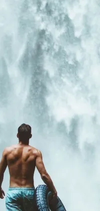 This phone live wallpaper features a man standing in front of a picturesque waterfall, holding a tire