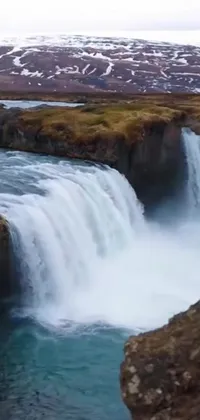 Indulge in the tranquility of nature with this phone live wallpaper featuring a mesmerizing waterfall against the backdrop of snow-capped mountains