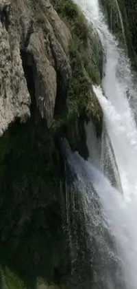 This phone wallpaper features a magnificent waterfall and a man standing on a rock beside it