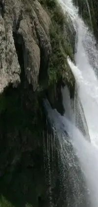 This live phone wallpaper is a nature lover's dream, featuring a stunning waterfall and a man perched atop a rock