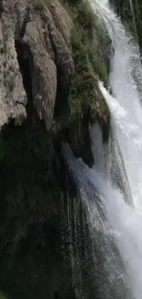 This phone live wallpaper depicts a thrilling scene of a man riding a wave atop a stunning waterfall