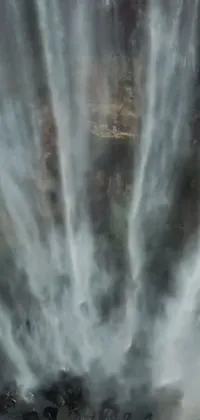 This phone live wallpaper features a stunning aerial shot of a waterfall with a group of people standing in front of it