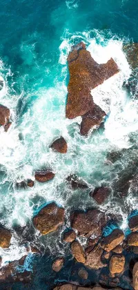 This phone live wallpaper offers a picturesque view of a body of water surrounded by rocks in a top-down perspective