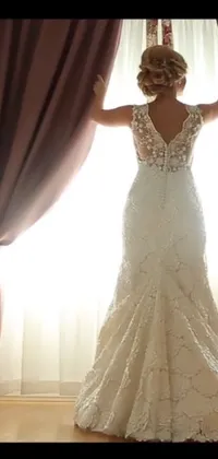 Looking for a stunning live wallpaper for your phone? Check out this romantic wallpaper featuring a bride in an elegant wedding dress standing in front of a backlit window
