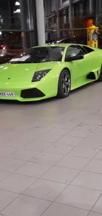 This phone live wallpaper showcases a sophisticated green sports car parked inside a contemporary building