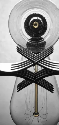 This phone live wallpaper showcases a mesmerizing surreal sculpture featuring a light bulb with forks sticking out of it, glass tableware pattern, and clock iconography