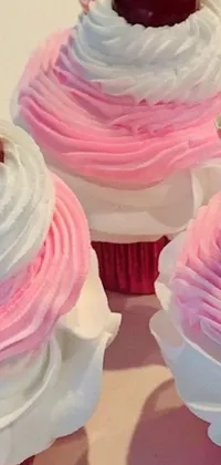 This live wallpaper features three cupcakes with pink frosting, whipped cream, and a cherry on top, all set against a two-tone pink and white background