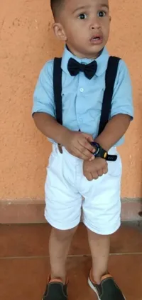 This cell phone live wallpaper showcases an adorable Colombian boy wearing a white uniform with bow tie and suspenders paired with blue shorts