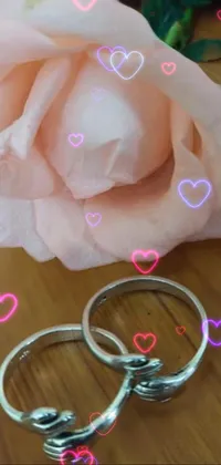 This stunning live phone wallpaper features two shining wedding rings and a beautiful rose on a table, forming a unique and mesmerizing hand gesture