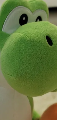 This phone wallpaper showcases a cute stuffed animal placed on a soft rug with a Yoshi picture in the background