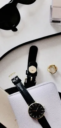 This phone live wallpaper features a minimalistic design with a black and white image of a purse sitting on a table beside a cell phone, with small vials and pouches on its belt