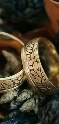 This unique phone live wallpaper features stunning wedding rings resting atop a rustic pile of pine cones