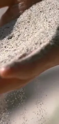 This live phone wallpaper displays a captivating close-up shot of hands holding sand in stunning detail