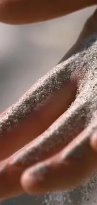 This phone live wallpaper captures a detailed close-up of sand held in a hand against a beautiful daylight backdrop