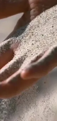 This phone live wallpaper depicts a ravishing close-up of a hand holding sand, captured in a moment of exhibition