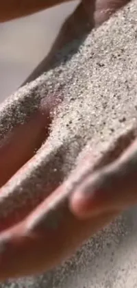 This live phone wallpaper features a close-up view of hands holding sand, creating mesmerizing kinetic pointillism effect
