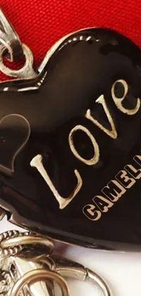 This phone live wallpaper showcases a stunning black heart-shaped pendant perched atop a bright red purse, adorned with the phrase &quot;I love you&quot; in delicate engraved letters