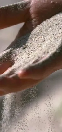 A stunning phone live wallpaper that features a close-up of a hand holding sand