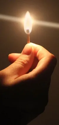 This phone live wallpaper features a candle with a flickering flame held in a person's hand against a dark background