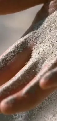 This live wallpaper features a mesmerizing close-up of a hand holding sand