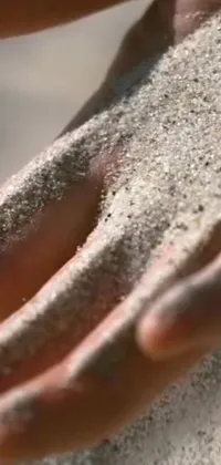 Get lost in the serenity of this phone live wallpaper depicting a close-up of a hand holding a handful of sand