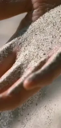 This phone live wallpaper features a captivating close-up shot of a hand holding sand