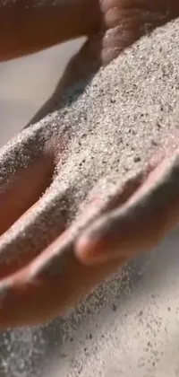This phone live wallpaper depicts a mesmerizing close-up of a hand holding sand in a unique kinetic pointillism style
