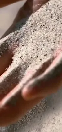 This live phone wallpaper captures a close up of sand in a person's hands