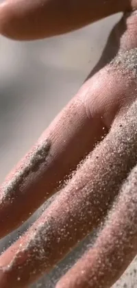 This phone live wallpaper captures the beauty of a close-up of a hand covered in sand