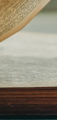 This phone live wallpaper features an open book on a wooden table