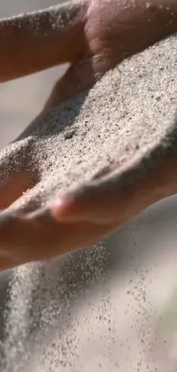 This mobile live wallpaper features a stunning close up of a person's hand holding golden sand
