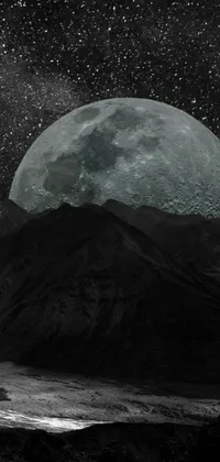 This phone wallpaper showcases a captivating black and white photograph of a full moon framed against a mountainous background, exuding an alluring gothic vibe