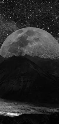 This live phone wallpaper showcases a mesmerizing black and white photograph of a full moon against a backdrop of mountains and stars