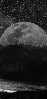 This live phone wallpaper showcases a mesmerizing black and white photograph of a full moon against a backdrop of mountains and stars