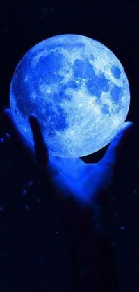 Adorn your phone with the captivating live wallpaper of a hand holding a glowing blue moon